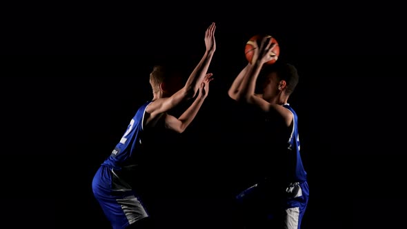 Two Young Sportsmen are Practicing Basketball in a Dark Studio on a Black Background