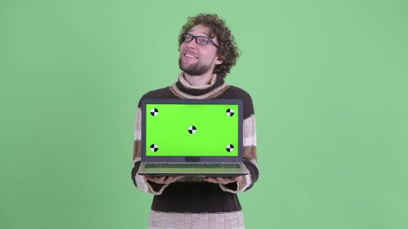 Happy Young Bearded Man Thinking While Showing Laptop