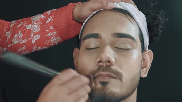 Young man in cosmetics studio and make up artist putting with make up brush powder on his face