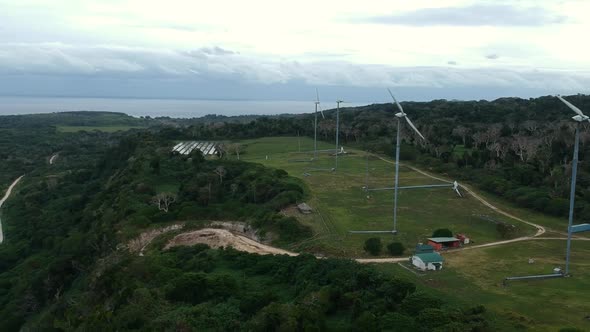 Aerial view of a wind and solar farm situated on a mountain top near the coastline of a tropical isl