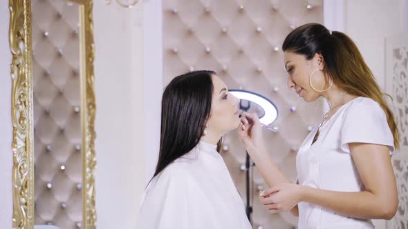 Makeup artist paints lips. Young woman undergoing procedure of lips makeup in salon