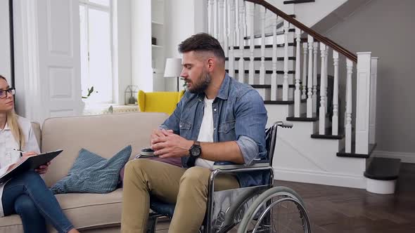 Bearded Man Sitting in Wheelchair and Talking with Attantive Female Medical