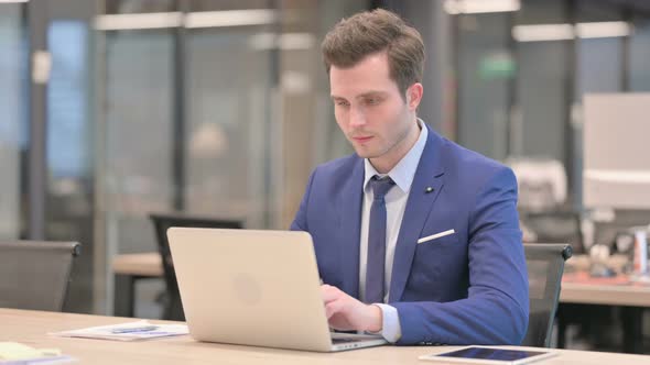 Businessman Showing Thumbs Up Sign While Using Laptop in Office