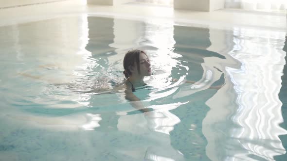 Young Brunette Caucasian Woman Swimming Along the Pool in Luxurious Spa Resort. Portrait of Joyful
