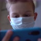 A Child in a Medical Mask Looks at the Phone - VideoHive Item for Sale