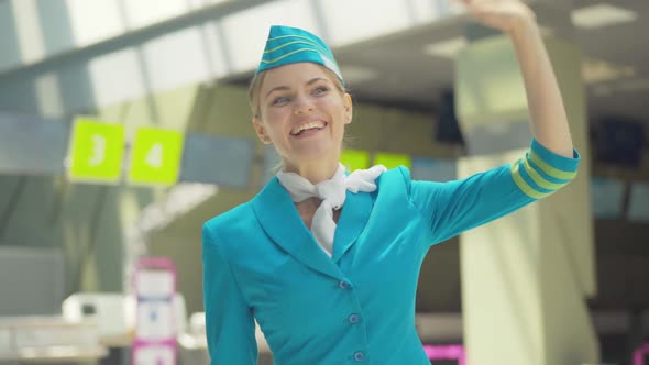 Portrait of Charming Caucasian Stewardess Waving in Airport. Beautiful Young Woman Smiling To