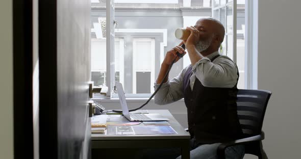 Businessman having coffee while talking on landline and using laptop at desk 4k