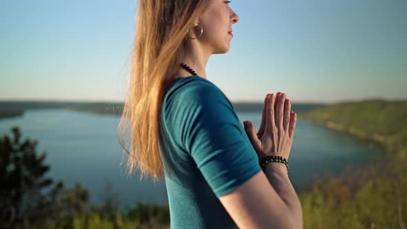 Woman Practicing Yoga Namaste Gratitude Mudra Alone on High Mountain Above River at Summertime