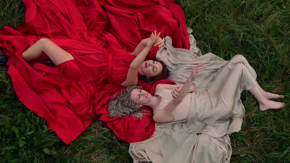 Fashion Photo of Two Beautiful Women in Long Dresses Lying on the Grass