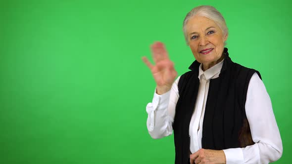 An elderly woman smiles and waves at the camera - green screen studio