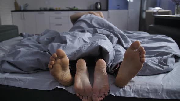 Feet of Affectionate Couple Cuddling in Bed