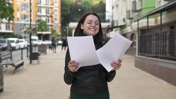 Woman on the street opens a paper letter, reads good news