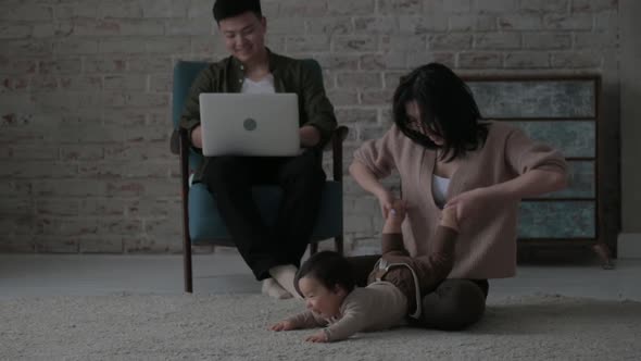 young mother sits on floor of cozy room inside house plays with crawling child