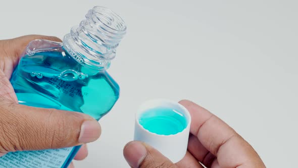 Hand Pouring Blue Mouthwash Into Cup