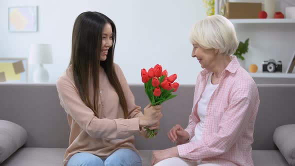 Beautiful Young Lady Presenting Bouquet of Flowers to Grandmother, Surprise