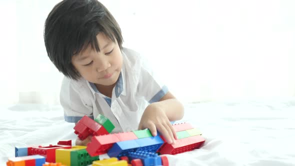 Little Asian Child Playing With Colorful Construction Blocks On White Bed