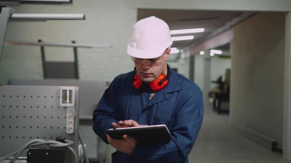 A Male Factory Worker Is Walking on the Workshop Using a Tablet