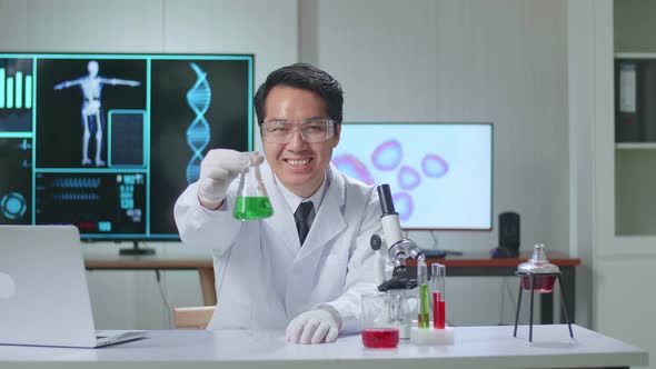 Young Asian Male Research Scientist Looking  Glass Test Tube And Warmly Smiles Into The Camera