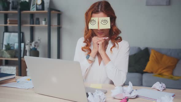 Tired Caucasian Woman Napping Sits at Table with Stickers on Eyes