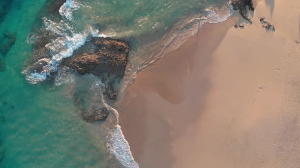 Summertime scenic flight directly above turquoise ocean sea water waves crashing on rocks by shoreli