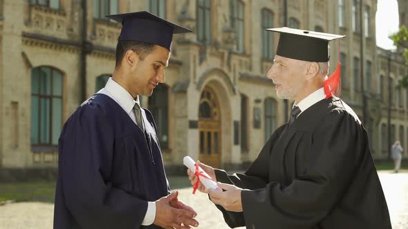 University Chancellor Giving Diploma to Male Student Shaking Hand Graduation Day