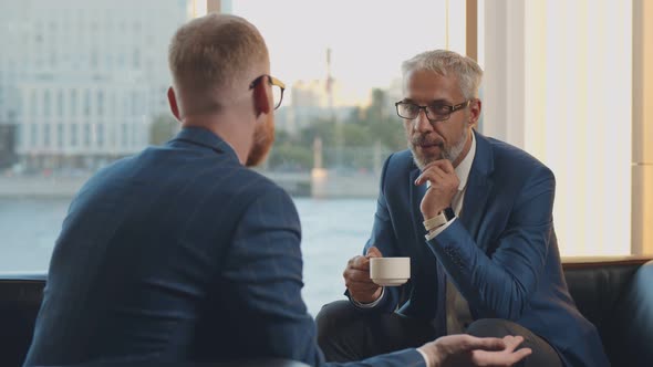 Colleagues Having Cheerful Conversation Sitting on Couch During Coffee Break in Office