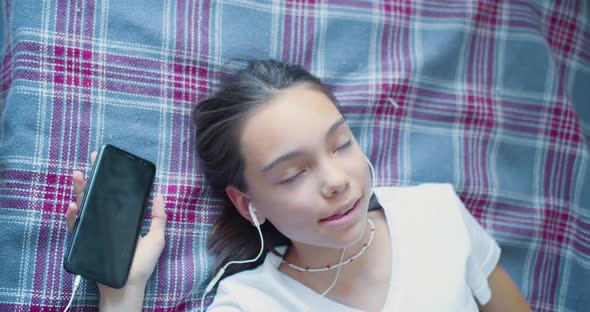 Teenage Girl Insert Earphones and Listening to the Music Via Online Smartphone App