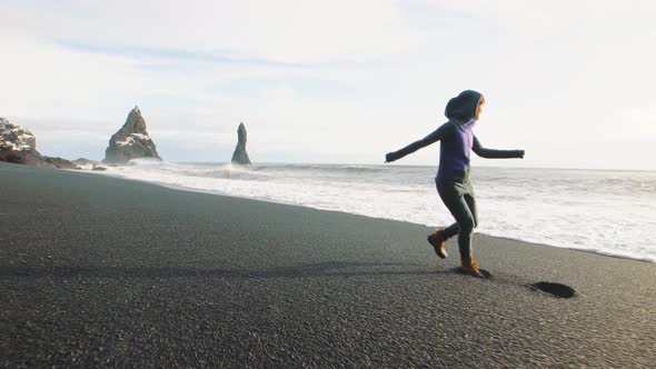 Hipster Woman Running on Volcanic Black Sand Beach in Iceland