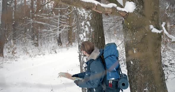 Man Standing in Forest During Snowfall and Looking at Map