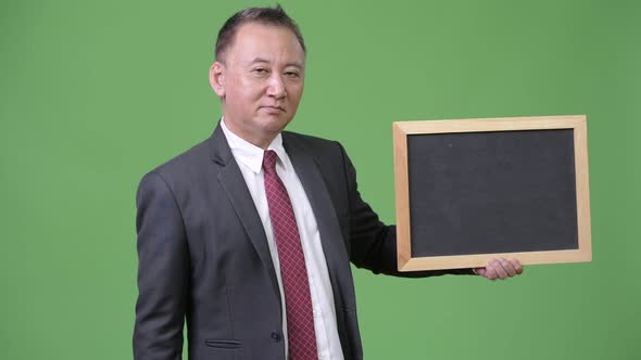 Mature Japanese Businessman Holding Blackboard Against Green Background