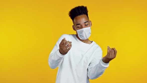 African Man in Protective Medical Mask Dancing Positive on Yellow Studio Background. Handsome Male