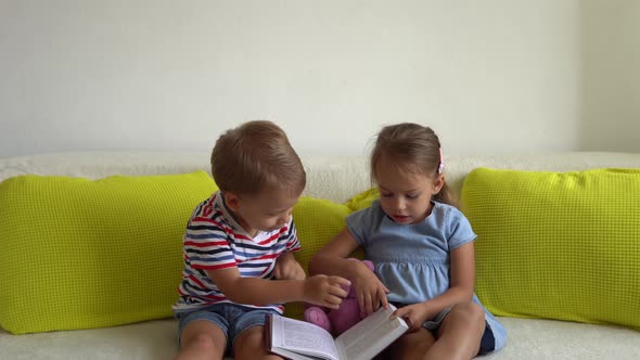 Two Cute Preshool Toddler Children Read Book of Fairy Tales On Couch