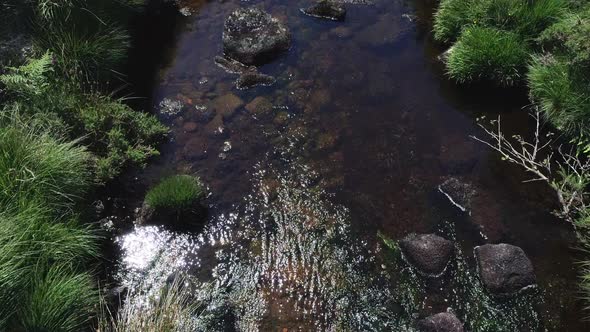 Birdseye close up aerial tracking forward of a rocky river following downstream surrounded by grassy