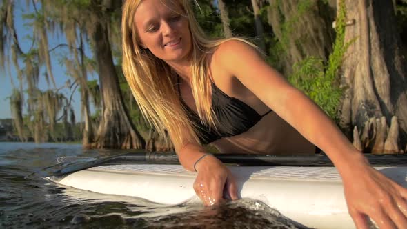 A young woman sitting on her board while sup stand-up paddleboarding on a lake.