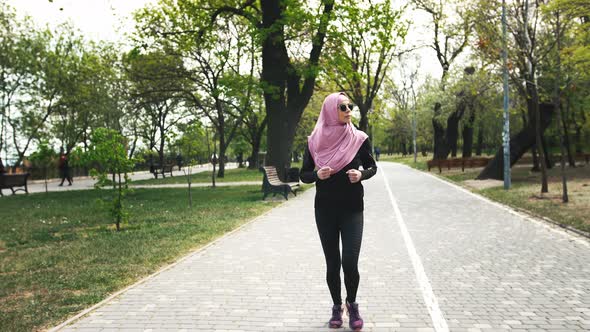 Young Modern Muslim Woman in Sunglasses and in Hijab Jogging in Green Park