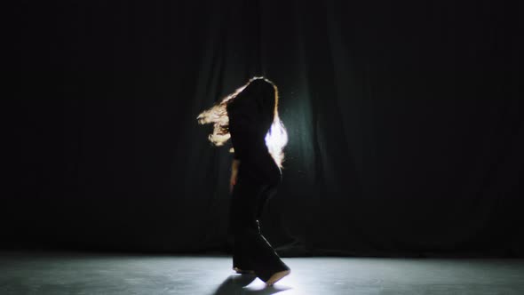 Active Gorgeous Graceful Girl with Long Curly Hair in Black Clothes in Dark Dance Studio on Stage in