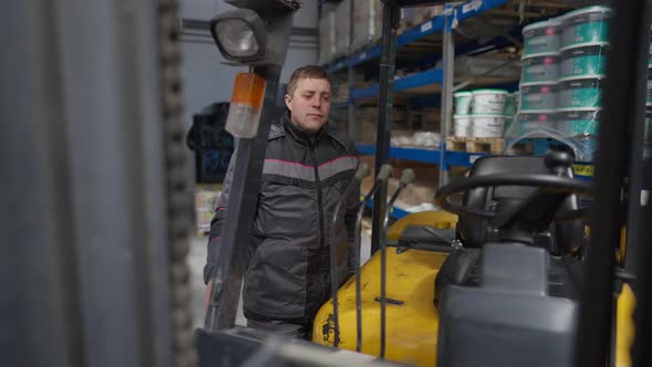 Portrait of Serious Caucasian Man in Uniform Looking at Camera and Sitting in Forklift in Slow