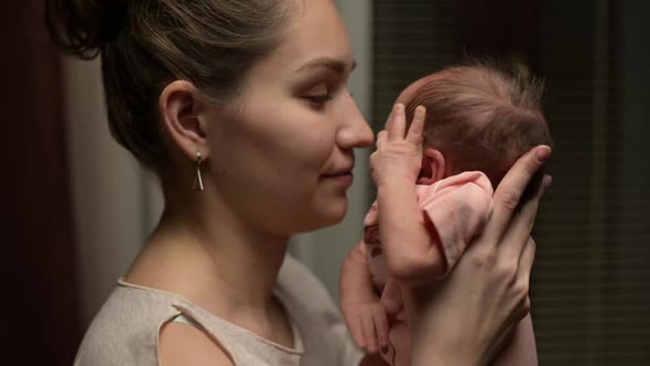 Young mother brings her newborn son to her face and caresses his face