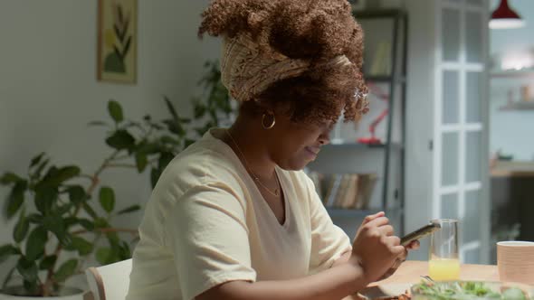 African American Woman Typing on Phone at Dinner Table