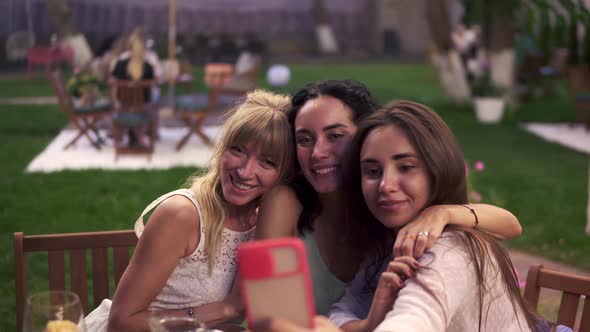 Carefree Women Chatting in Veranda Cafe Outdoors Taking Selfie Photo or Video on Smartphone