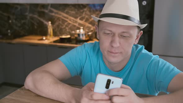 Portrait of an Attractive Man Who in a White Hat Sits at a Table Uses a Mobile Phone