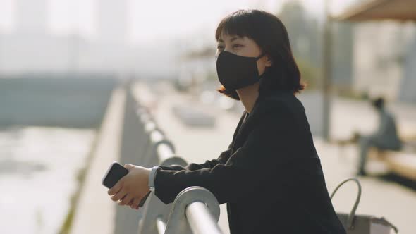 Asian Businesswoman in Mask Standing on Embankment in City