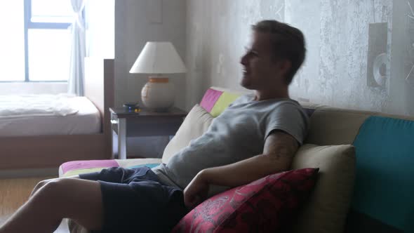 Handsome Young Man at Home Sitting on a Couch Watches TV Some Comedy