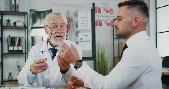 Man Taking Bottles with Pills From Experienced Responsible bearded senior doctor