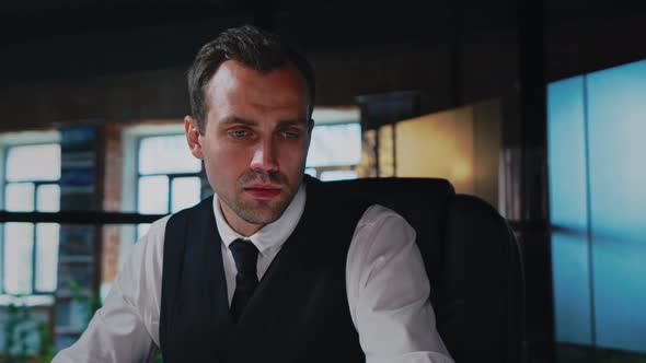 A Man Sits at a Table in the Office Works with a Computer and Documents