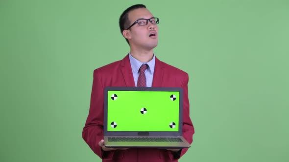 Happy Asian Businessman Thinking While Showing Laptop