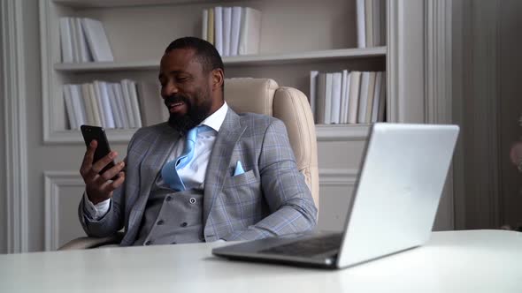 a Bearded AfricanAmerican Man in a Plaid Suit with a Tie is Sitting at a Table on a Light Chair and
