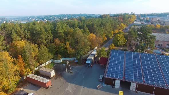 View from above on the road with trucks near green park. Building with solar energy panels in the co