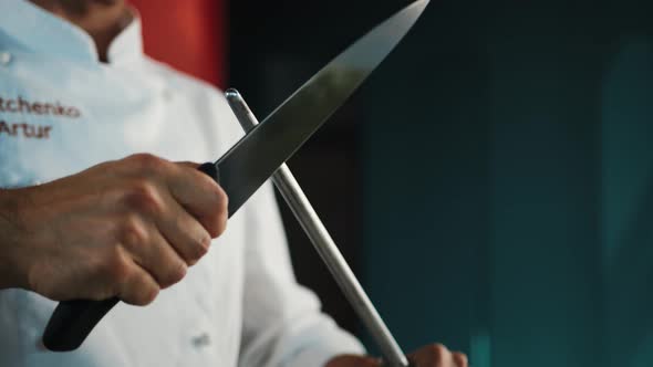 Restaurant kitchen: male chef sharpening knives before cooking steak