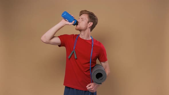Handsome Man with Yoga Mat Drinking Water on Beige Background